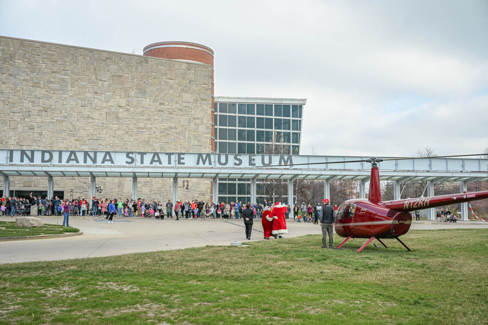 Santa standing beside a red helicopter in front of a crowd outside the Indiana State Museum.